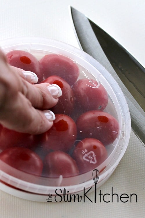 a hand holding grape tomatoes on a lid with a knife