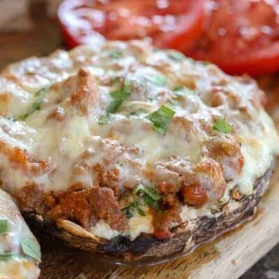 Lasagna Stuffed Mushrooms on a wood board with tomatoes in the background