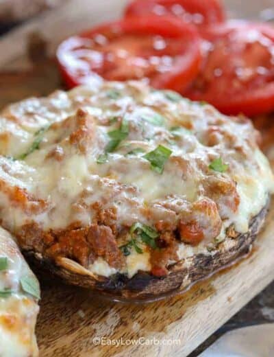 Lasagna Stuffed Mushrooms on a wood board with tomatoes in the background