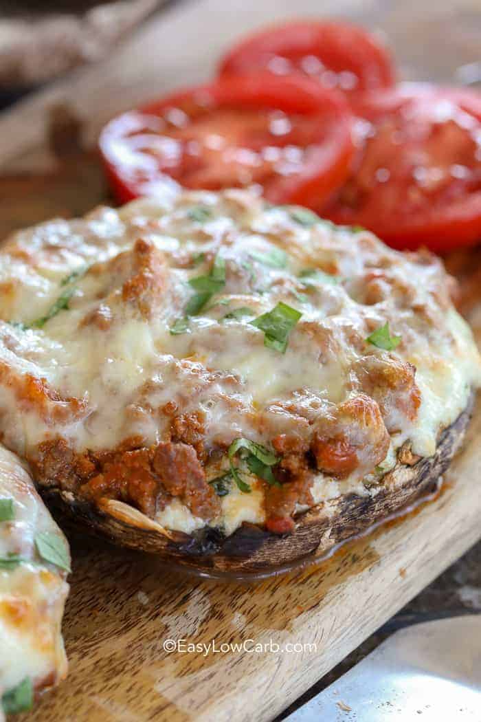 Lasagna Stuffed Mushrooms on a wood board with tomatoes in the background