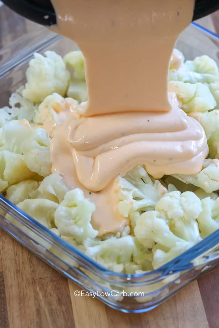 pouring cheese sauce on Low Carb Creamy Cauliflower Casserole