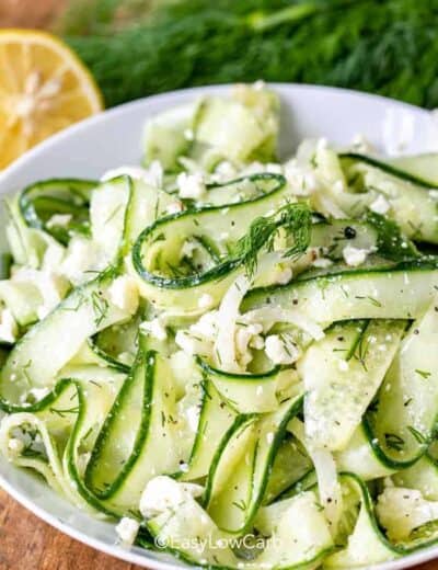 Cucumber Feta Salad in a white bowl, with dill and lemon in the background
