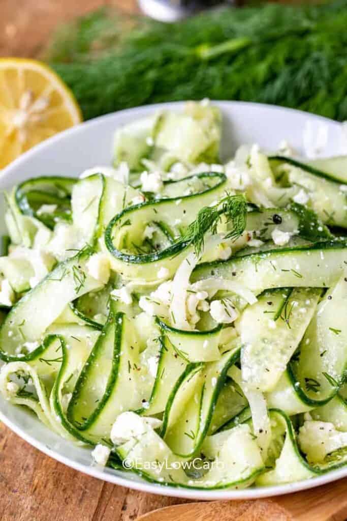 Cucumber Feta Salad in a white bowl, with dill and lemon in the background