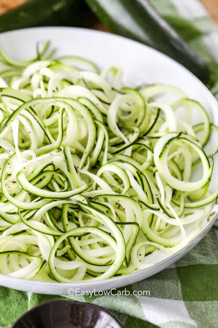 side view of zoodles in a white dish with zucchini in the background