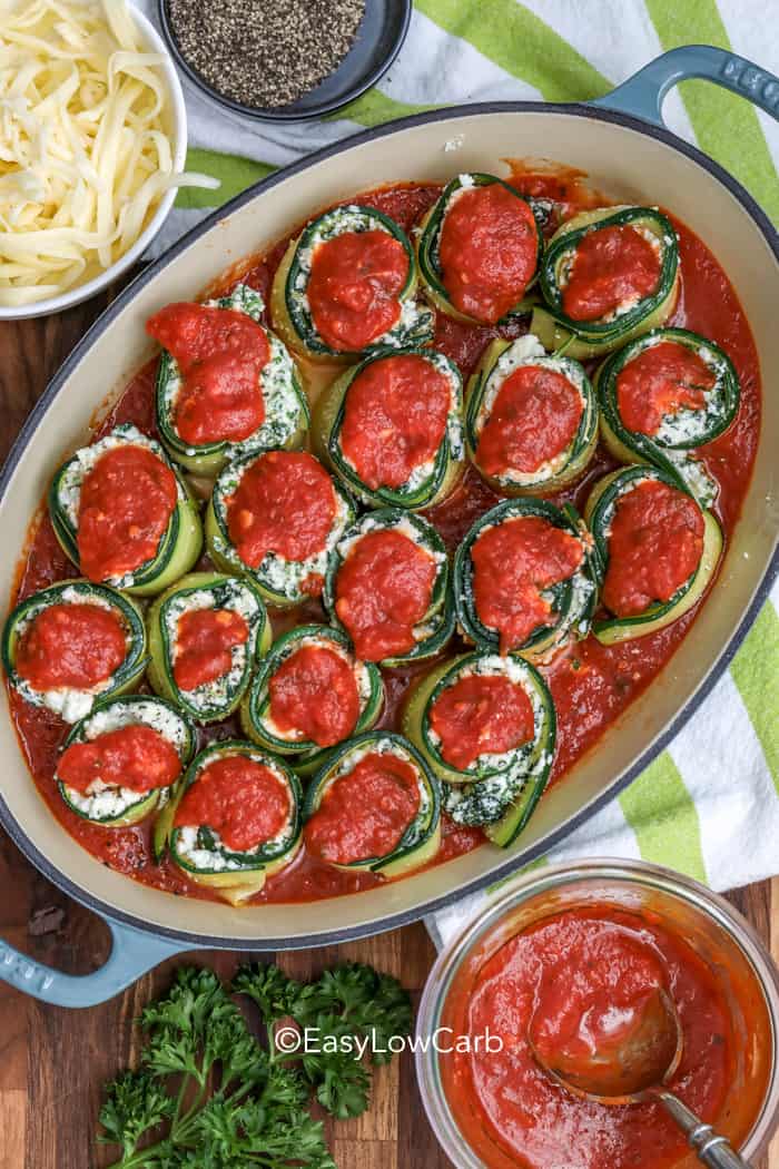 prepping Zucchini Lasagna Roll Ups in a baking dish with sauce on the top