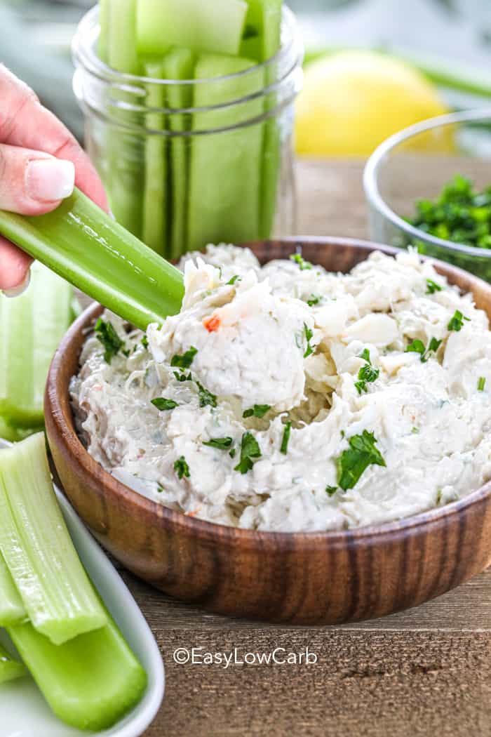 dipping celery into low carb crab dip in a wood bowl