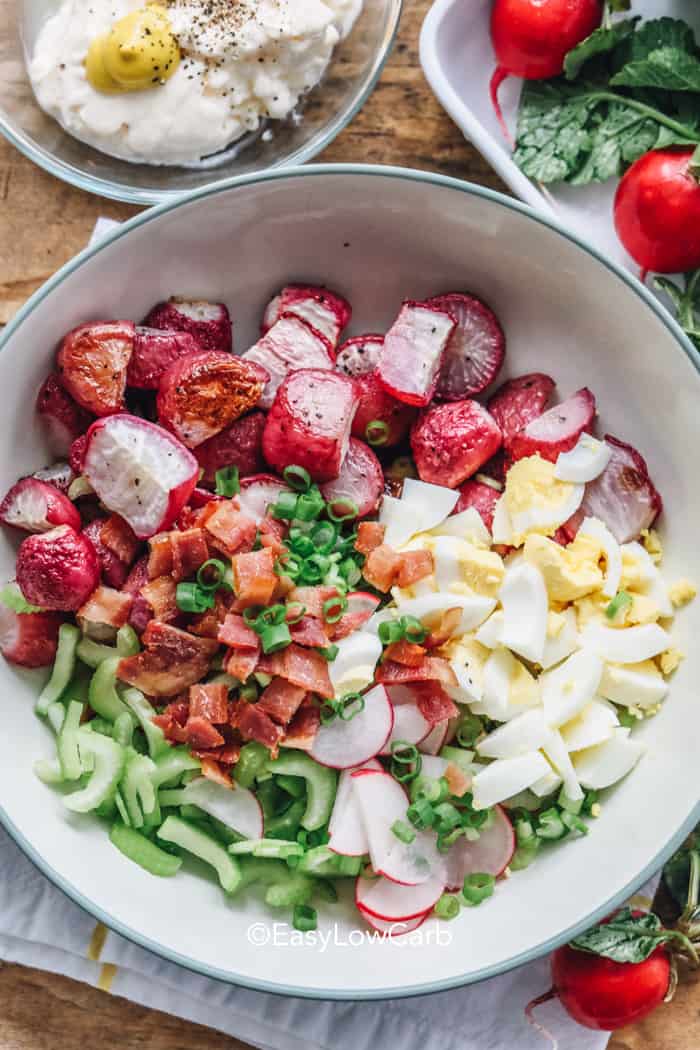 Radish potato salad is a simple way to add bold flavor to any meal. Tender roasted radishes are tossed in a creamy garlic dressing with bacon, celery, eggs, green onions, and pickles for a classic chilled salad everyone loves. It is ideal for BBQ spreads, weeknight dinners, and low carb meal plans when you want something satisfying yet lighter than traditional potato salad. One scoop is never enough. #easylowcarb overhead of radish salad ingredients