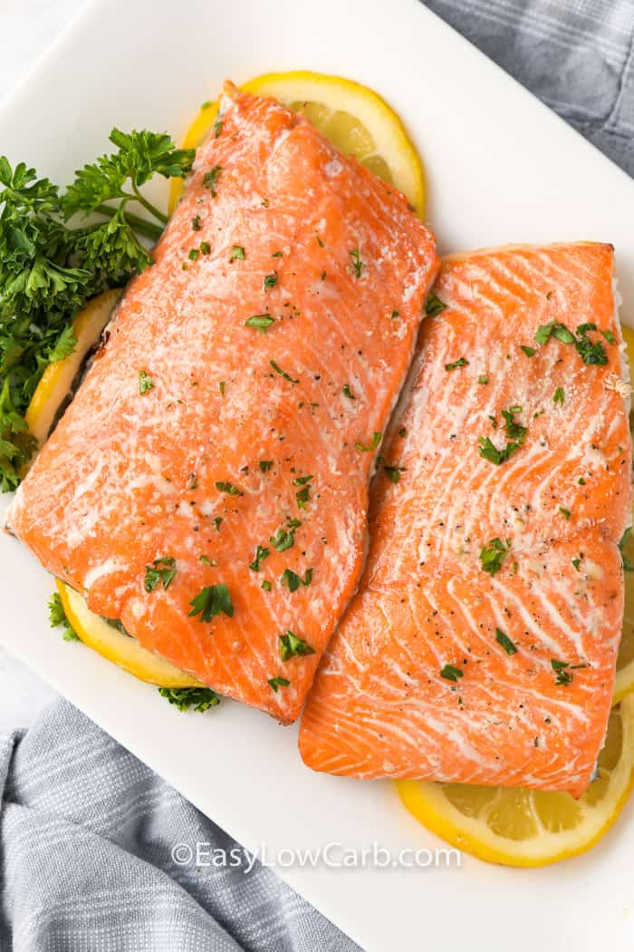 Salmon in the air fryer on a white plate with garnish and lemons