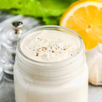 Easy Caesar Salad Dressing in a jar with lemon , garlic , lettuce and salt and pepper behind it