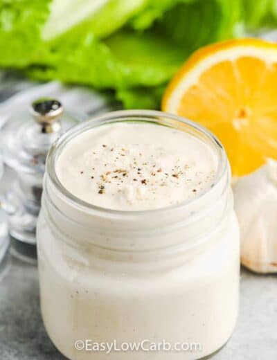 Easy Caesar Salad Dressing in a jar with lemon , garlic , lettuce and salt and pepper behind it