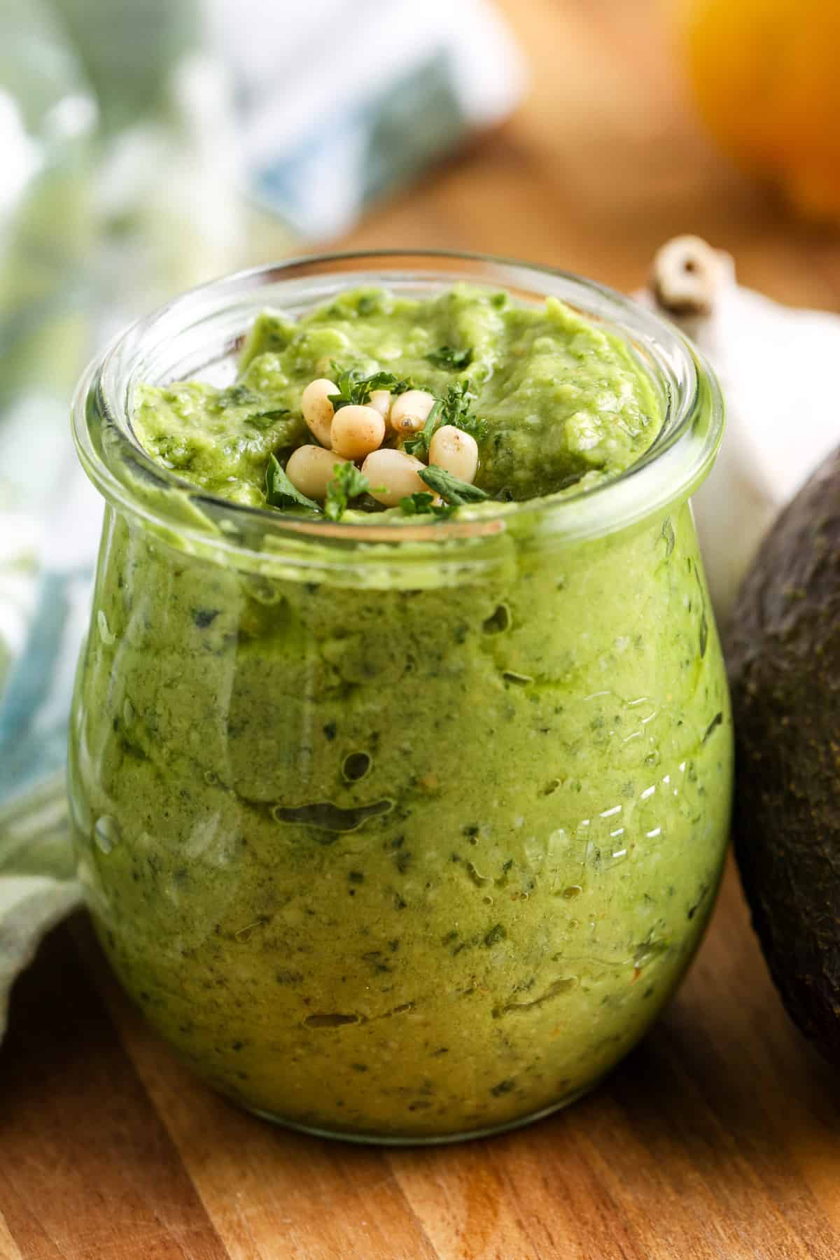close up of Avocado Pesto in a jar with an avocado