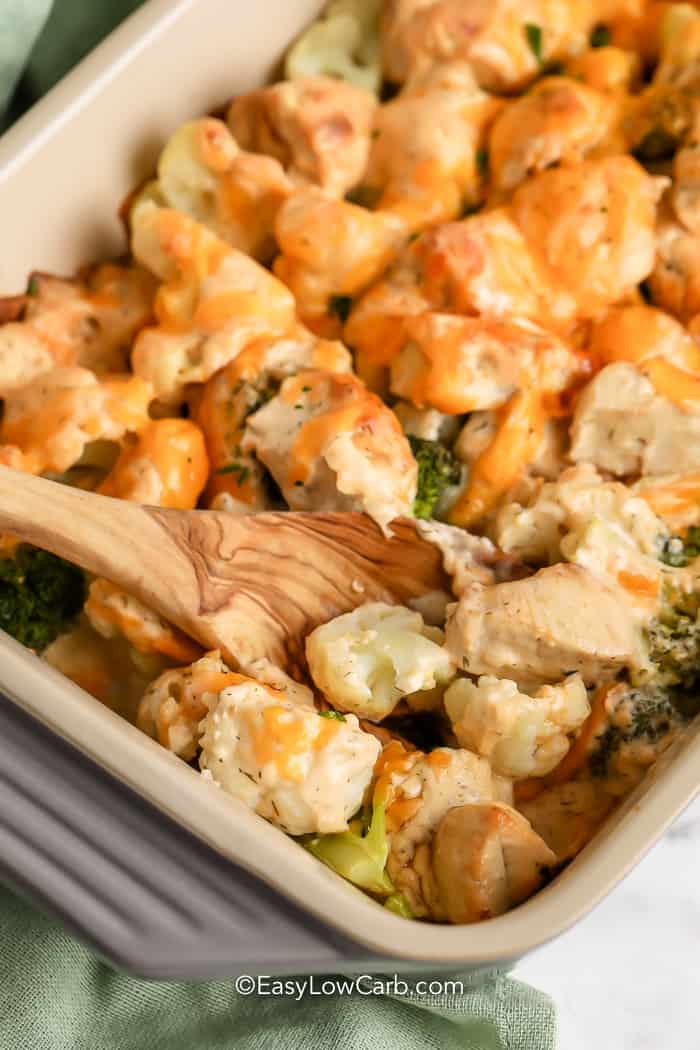 wooden spoon scooping Chicken Broccoli Cauliflower Casserole in a pan