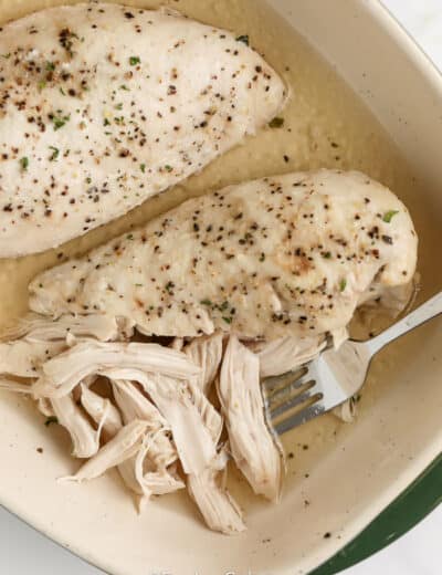 cooked shredded chicken in a casserole dish with one breast partially shredded