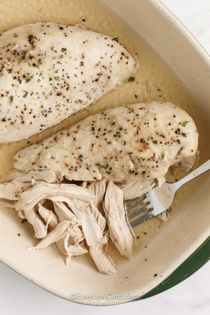 cooked shredded chicken in a casserole dish with one breast partially shredded