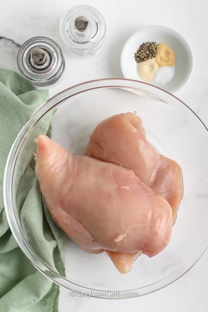 raw chicken breasts for shredded chicken in a glass bowl with seasoning ingredients beside it