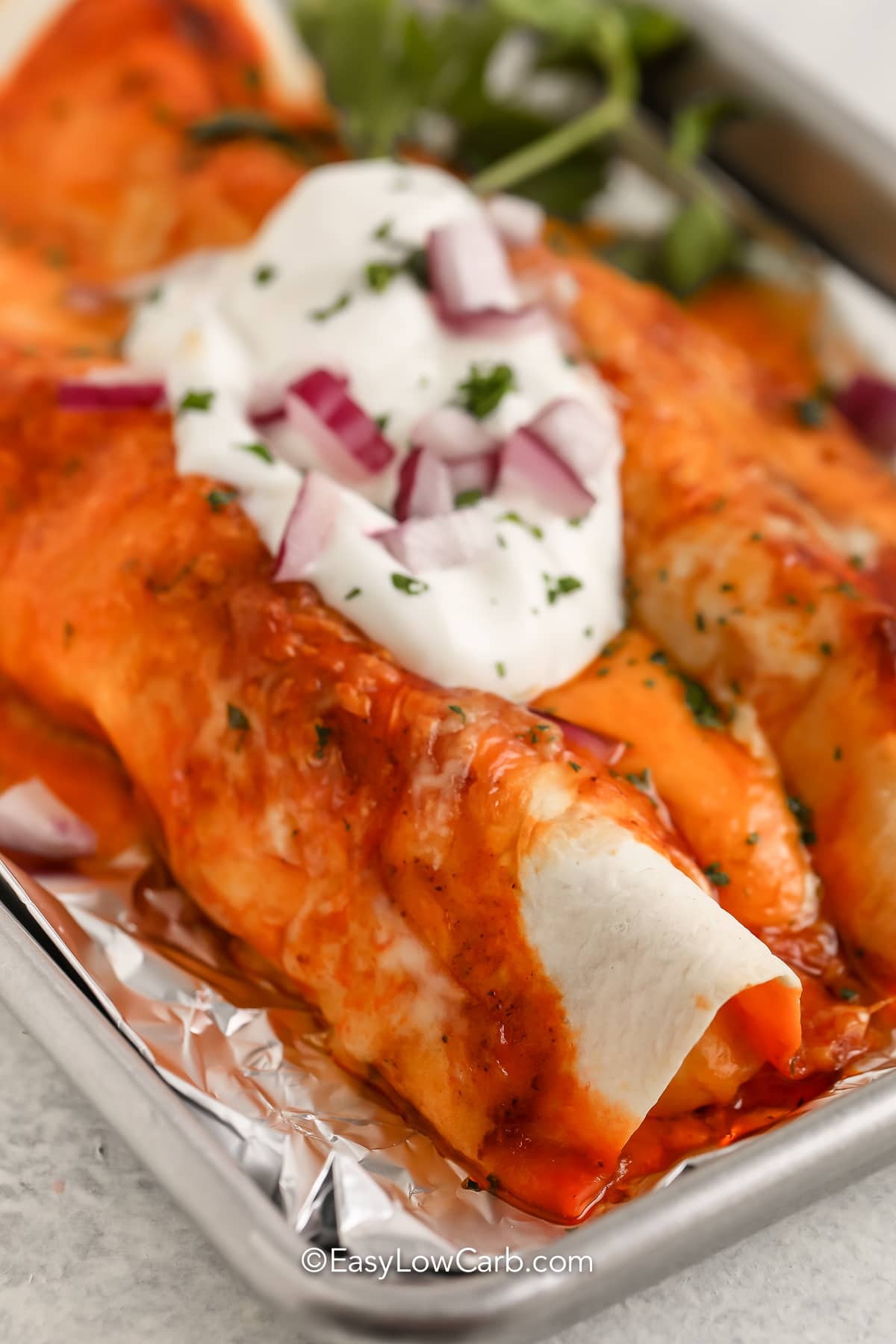 Low Carb Enchiladas baked in a pan with sour cream and red onion on top.