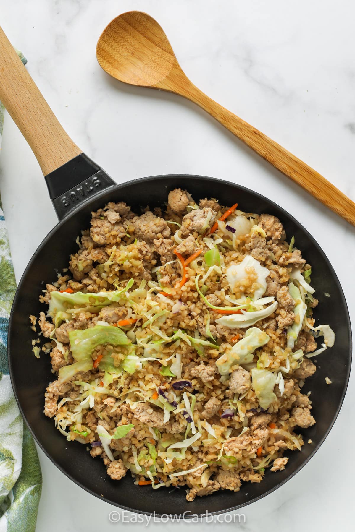 This low carb cabbage stir fry is perfect for busy nights because the prep is almost done for you. Bagged slaw and frozen cauliflower rice cook quickly with ground chicken, garlic, and ginger. The seasoning stays simple and flexible with liquid aminos or soy sauce, plus toasted sesame oil for aroma. It reheats well for lunches and makes an easy bowl meal with optional green onions and peanuts. #easylowcarb Easy Stir Fry Chicken and Vegetables in a skillet with a wooden spoon