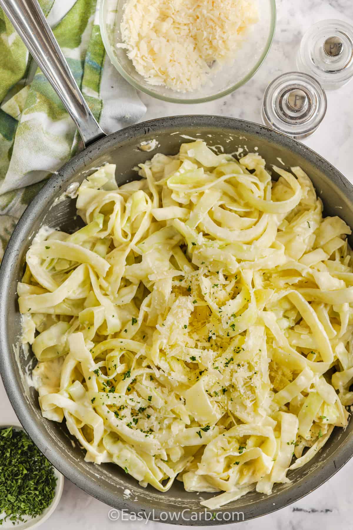 Cabbage Noodles Alfredo in a frying pan with parmesan and parsley on the side