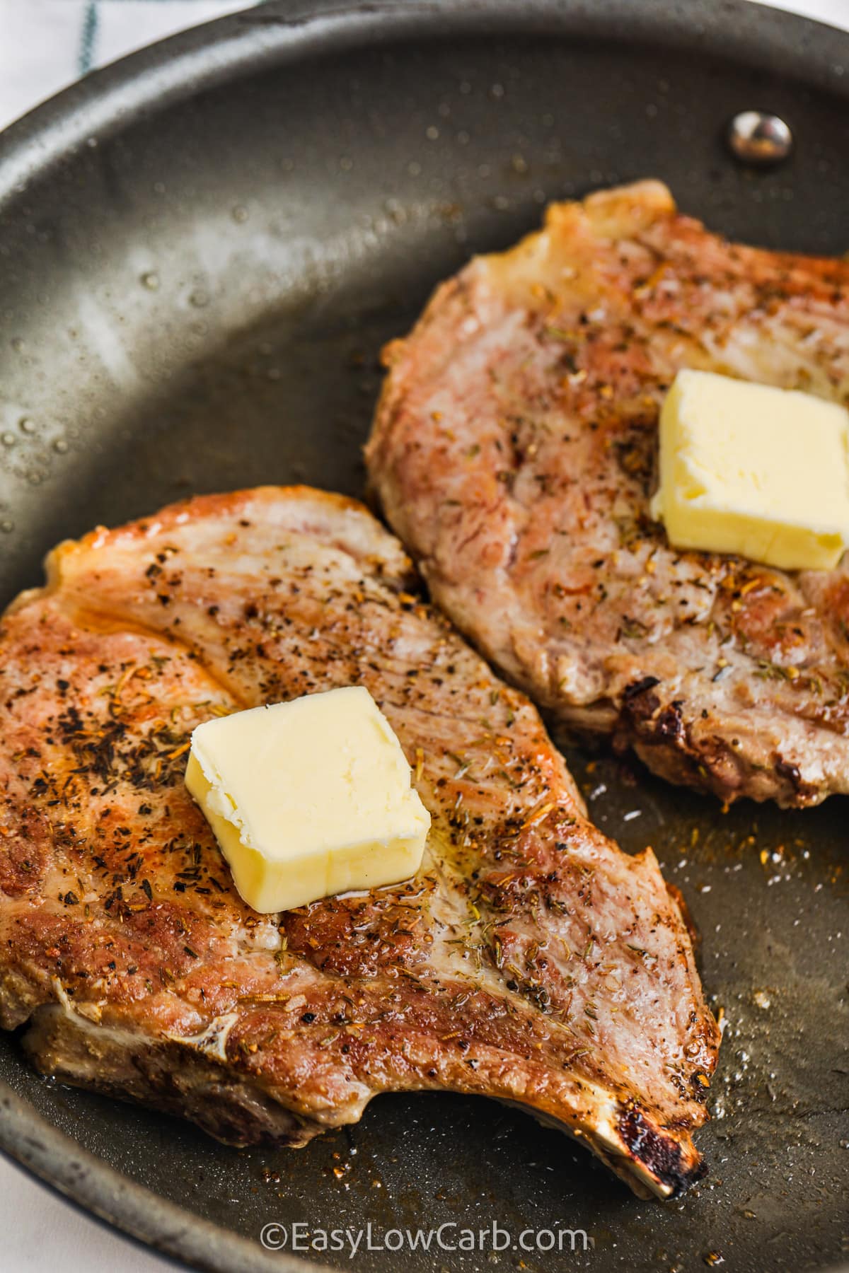 Pan Seared Pork Chops in a pan with pats of butter