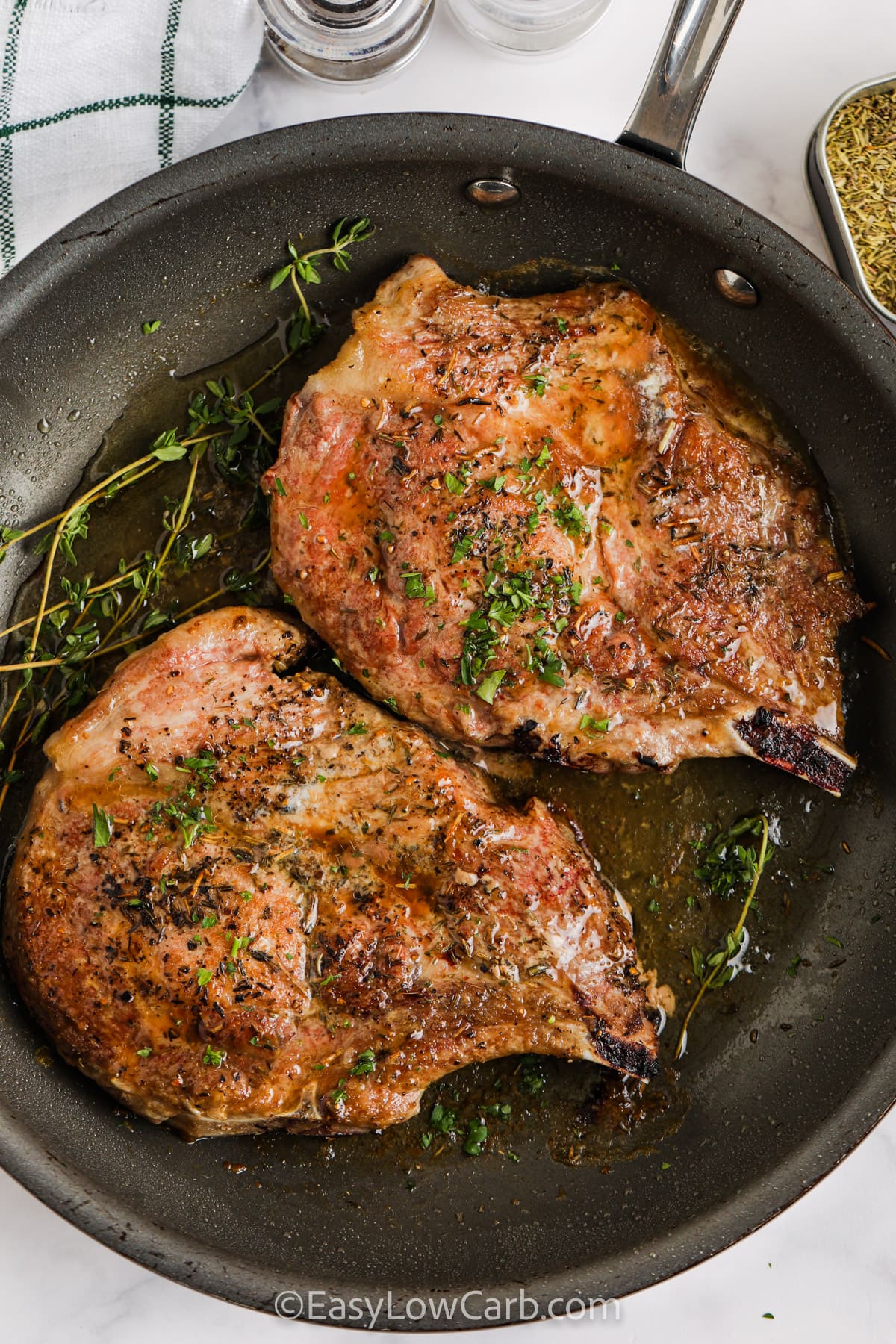 Pan Seared Pork Chops in a pan with thyme and parsley