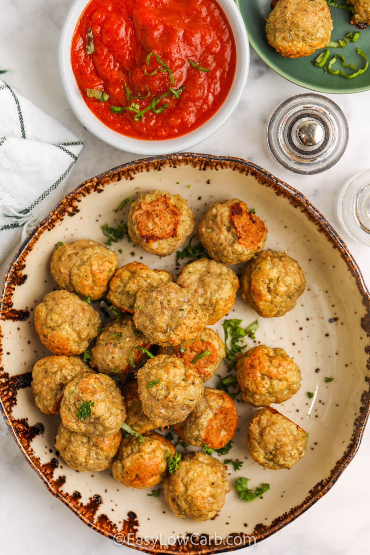 Make these oven baked chicken meatballs on a single sheet pan for a fast, low carb dinner that is easy to clean up. The recipe uses ground chicken, parmesan, garlic, and almond flour to create juicy meatballs with Italian flavor and no breadcrumbs. They are delicious with marinara and veggie noodles or served with roasted vegetables on the side. Freeze extras for later, and you will always have a simple protein ready to go. #easylowcarb Chicken Meatballs on a plate with a side of marinara