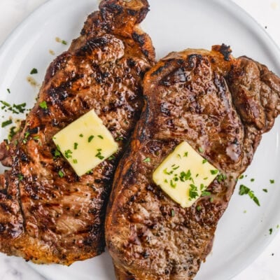 Grilled Striploin on a white plate with butter and a fresh parsley garnish