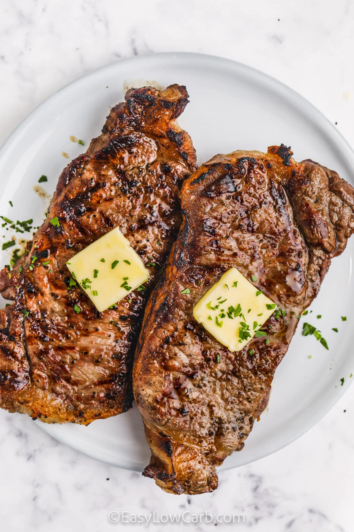 Grilled Striploin on a white plate with butter and a fresh parsley garnish