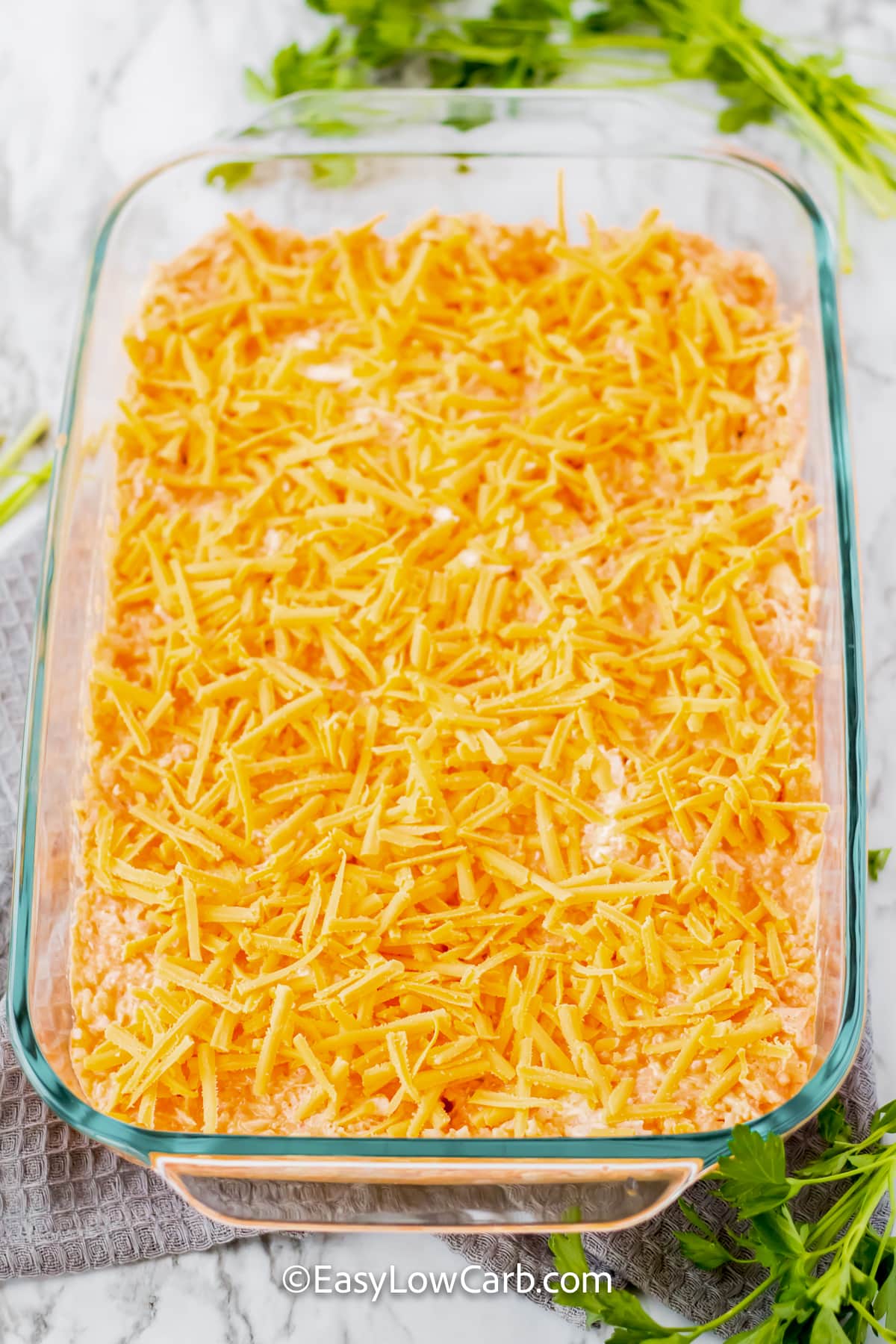 Make keto buffalo chicken casserole when you want an easy dinner with bold flavor. Buffalo sauce gives the chicken and cauliflower rice a spicy kick, while cream cheese and sour cream add creamy richness. Cheddar on top brings everything together in a hearty low-carb casserole. It is a great recipe for leftover chicken and can be prepared ahead for a convenient meal. Add this cheesy chicken casserole to your menu today. #easylowcarb keto buffalo chicken casserole mixture in a dish topped with cheese.