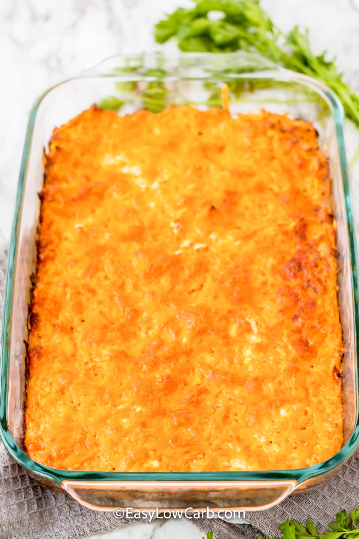 Keto buffalo chicken casserole is loaded with the spicy, creamy flavors of classic buffalo chicken. Shredded chicken and cauliflower rice make the filling hearty, while cream cheese and sour cream add rich flavor. Eggs help bind everything together, and cheddar creates a deliciously cheesy topping. Add blue cheese and green onions before serving for an extra burst of flavor. Try this easy low-carb casserole for a comforting dinner. #easylowcarb baked keto buffalo chicken casserole in a dish.
