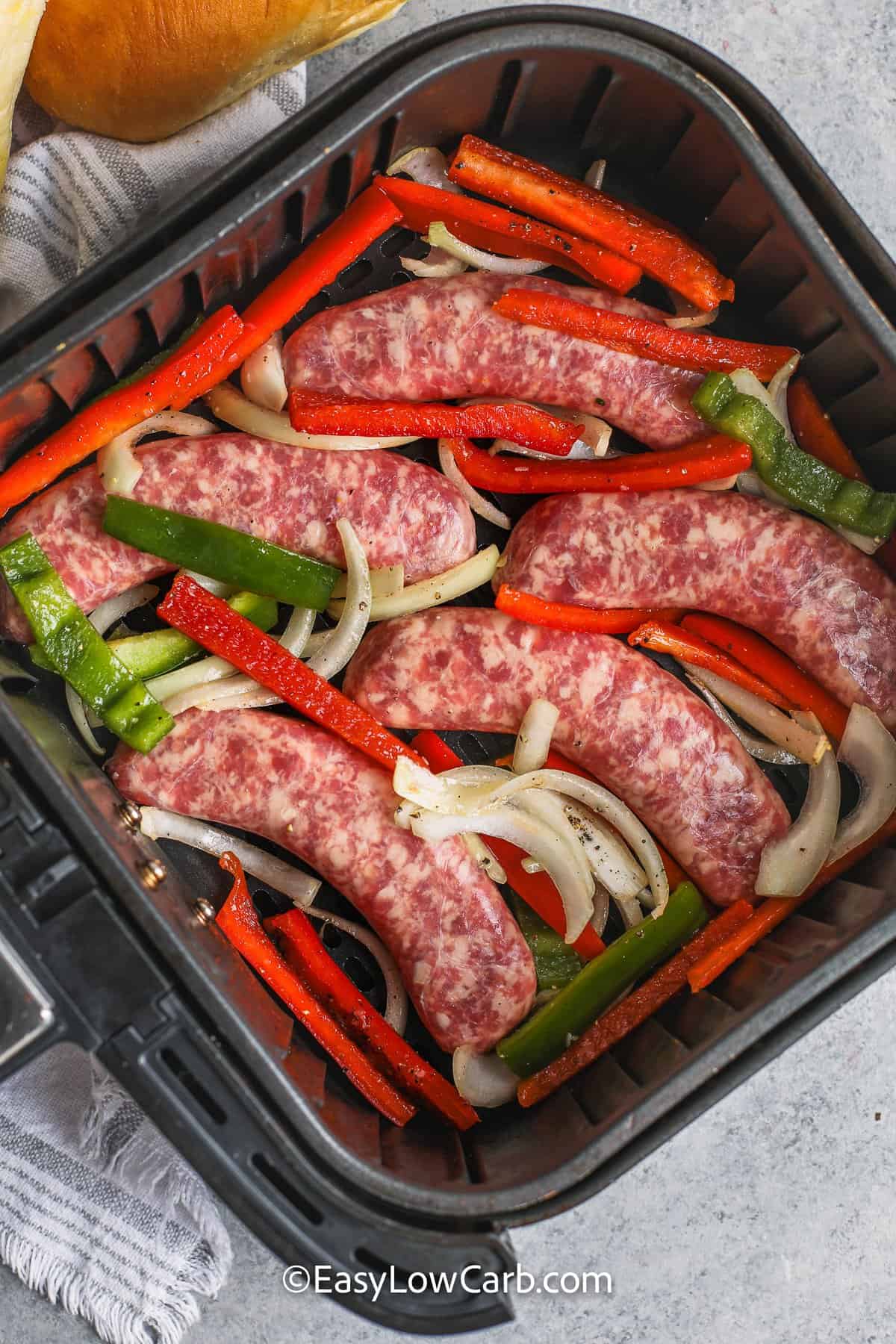 uncooked brats with peppers and onions in an air fryer tray