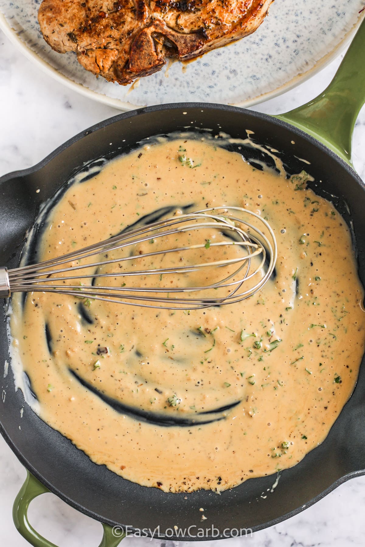 sauce in a skillet with a whisk for Creamy Skillet Pork Chops