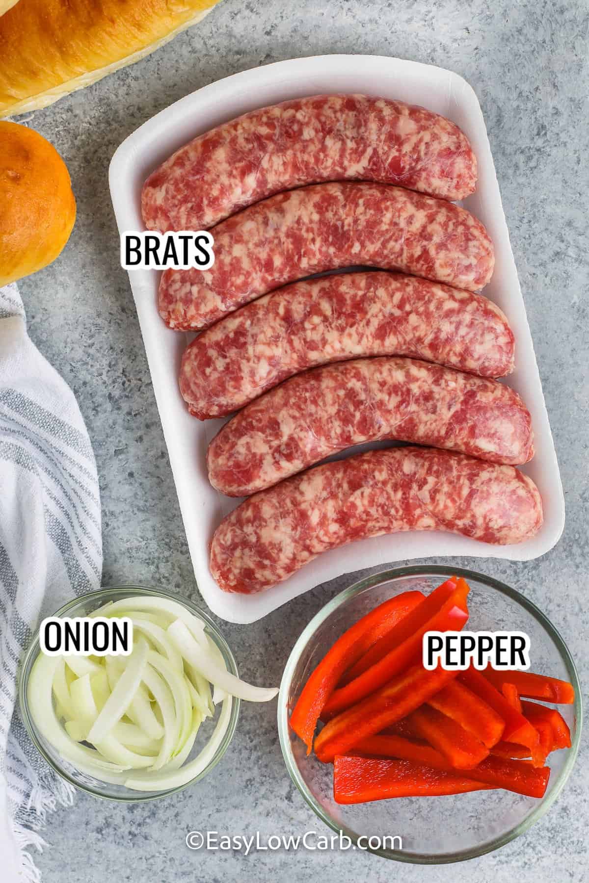 ingredients assembled to make brats with peppers and onions including brats, onions, and peppers
