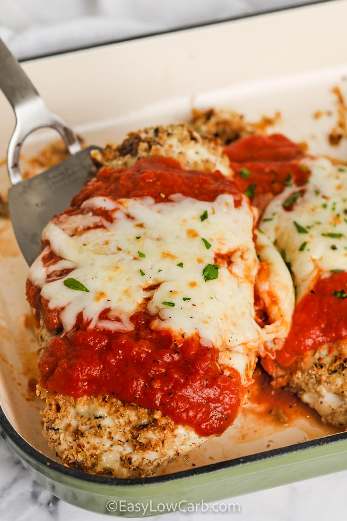 taking a piece of Low Carb Baked Chicken Parmesan out of the dish