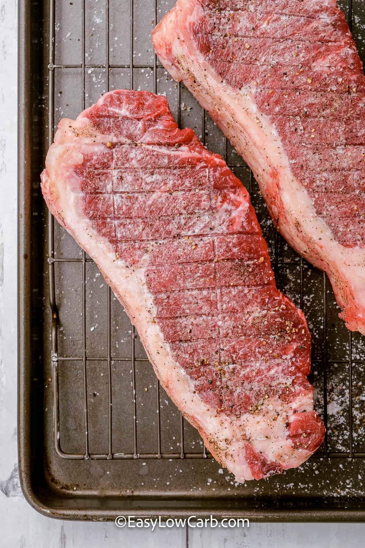 seasoned raw New York strip steaks on a grill