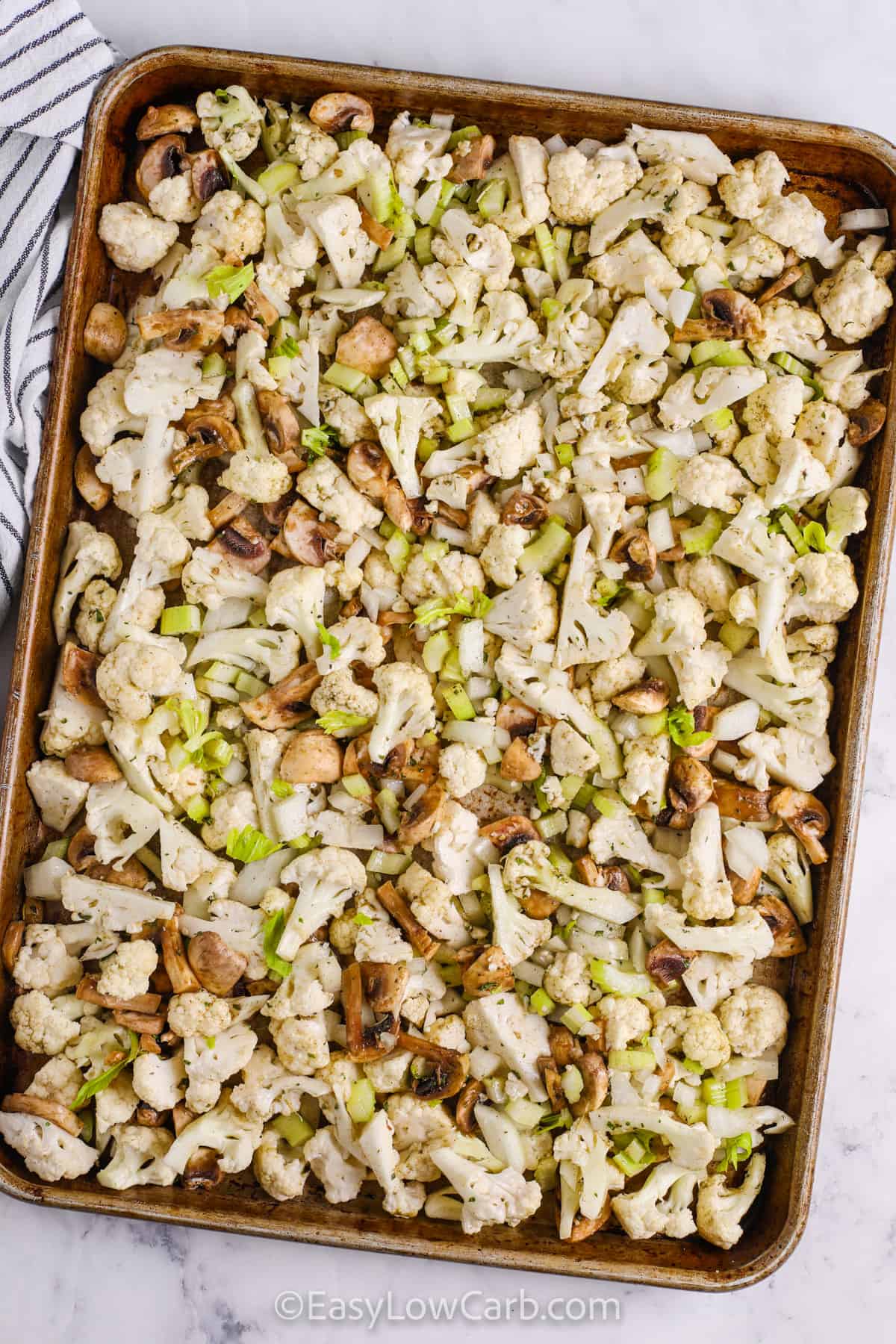 Roasted cauliflower stuffing brings classic stuffing flavor to a vegetable-packed side without relying on bread. Small cauliflower florets, mushrooms, celery, and onion roast with butter, poultry seasoning, parsley, and rosemary for a tender center and flavorful golden edges. It is easy enough for Sunday dinner and festive enough for Thanksgiving or Christmas. Save this cauliflower stuffing recipe for your next cozy dinner. #easylowcarb ingredients on a sheet pan to make Cauliflower Stuffing.