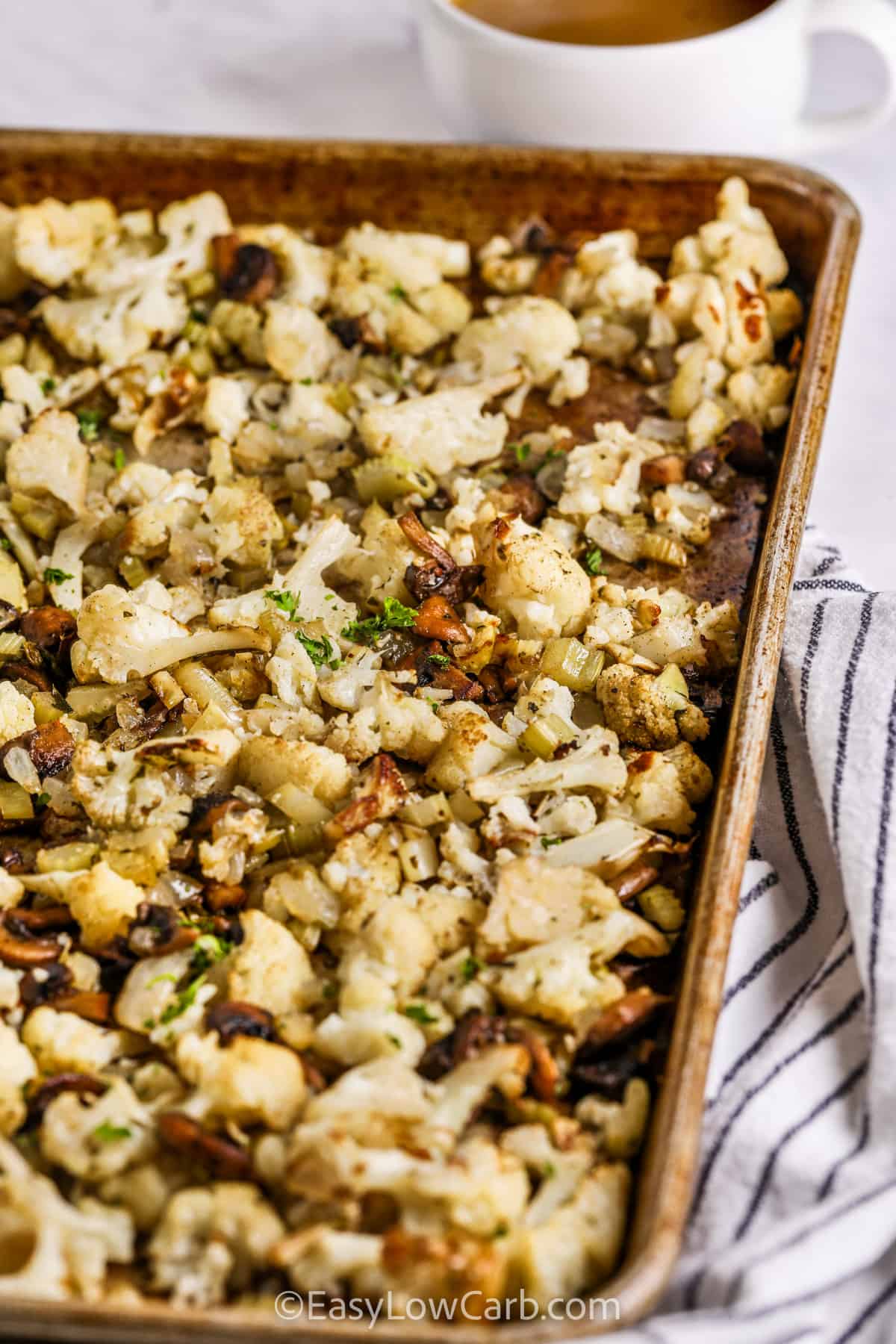 This cauliflower stuffing recipe turns everyday vegetables into a warm, savory side that fits right into a holiday menu. Cauliflower and mushrooms develop deeper flavor as they roast, while celery and onion add familiar stuffing character. Butter, rosemary, parsley, and poultry seasoning pull everything together with cozy flavor in every bite. Keep this low carb holiday side handy and save the recipe for your next roast dinner. #easylowcarb cooked Cauliflower Stuffing on a sheet pan.
