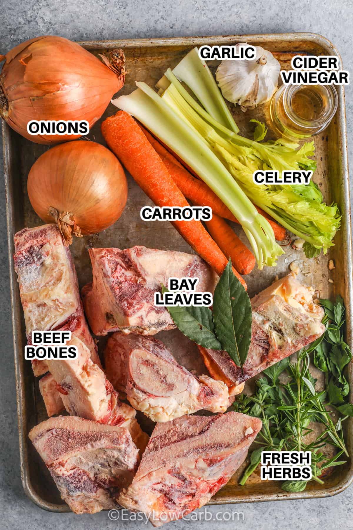 ingredients to make a beef bone broth recipe, including onions, celery, carrots, garlic, cider vinegar, beef bones, bay leaves and fresh herbs