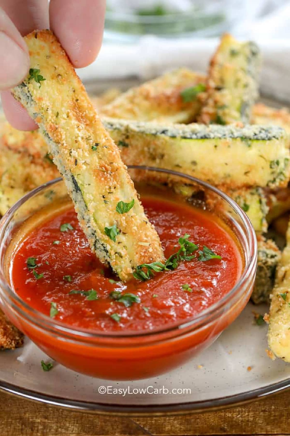 keto zucchini fries on a plate, with one fry dunked into marinara sauce