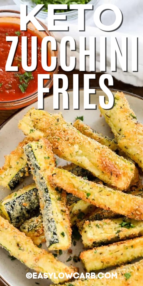 baked keto zucchini fries piled on plate with a small bowl of marinara sauce in the background, with a title