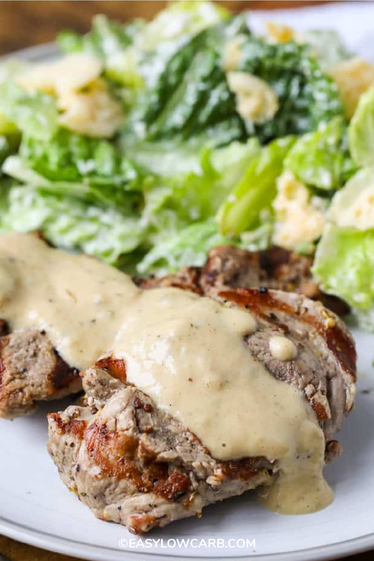 Creamy Dijon Pork Medallions on a white plate with salad in the background