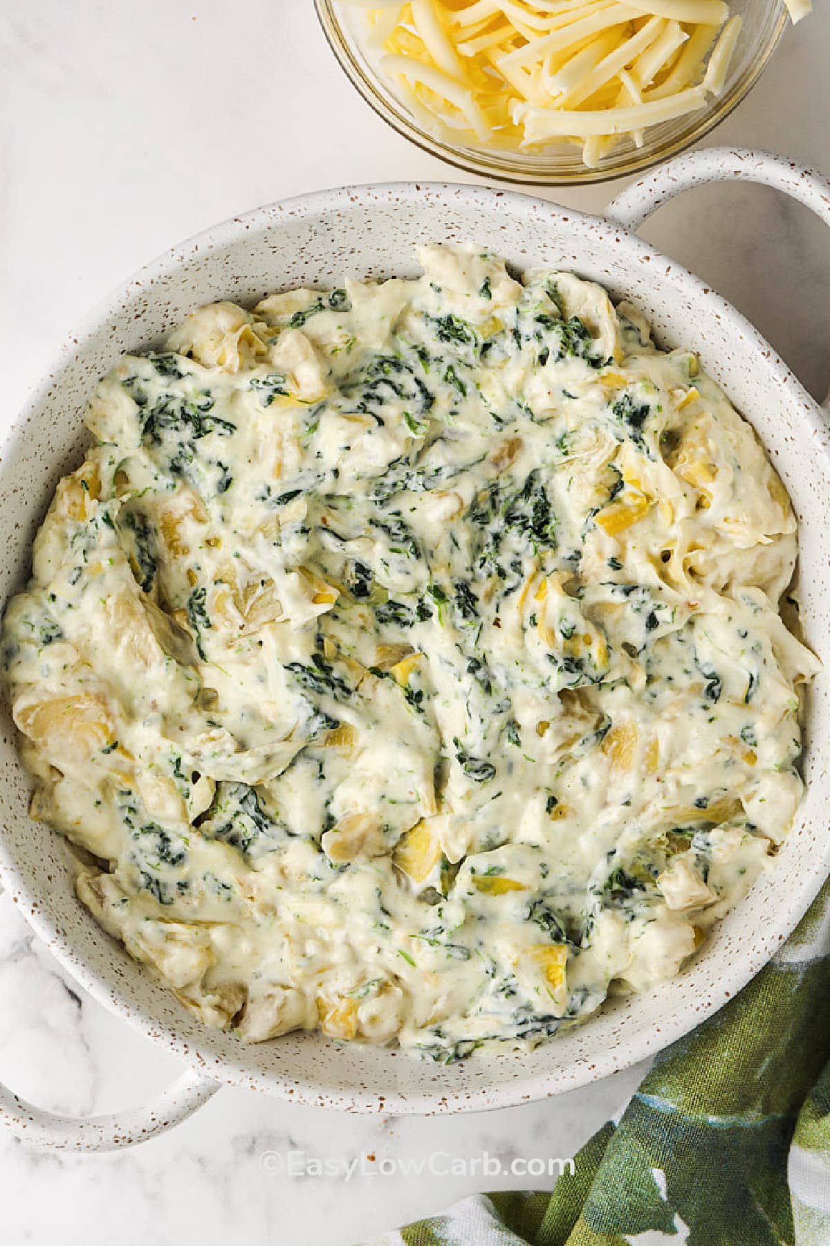 artichoke spinach dip in a dish before topped with cheese and baked
