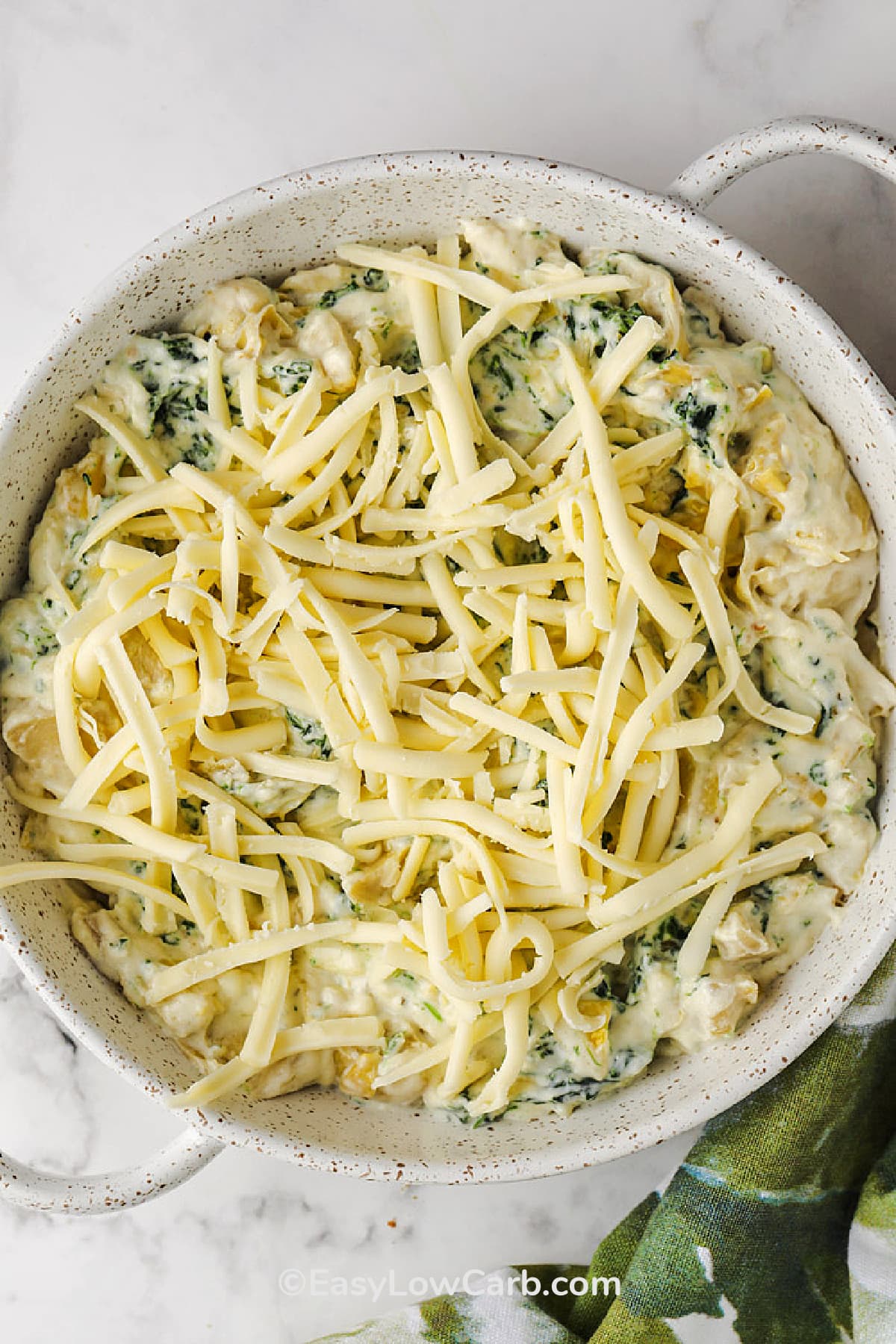 uncooked artichoke spinach dip in a dish, topped with cheese