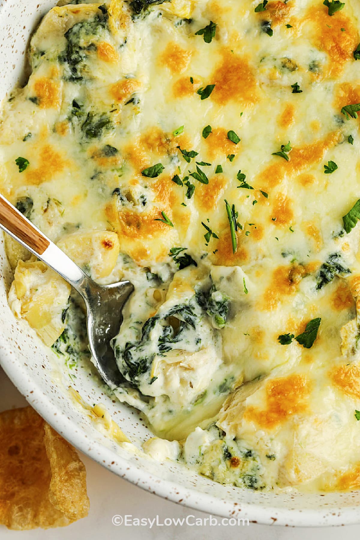 baked artichoke spinach dip in a dish with a spoon in the dip, ready to serve