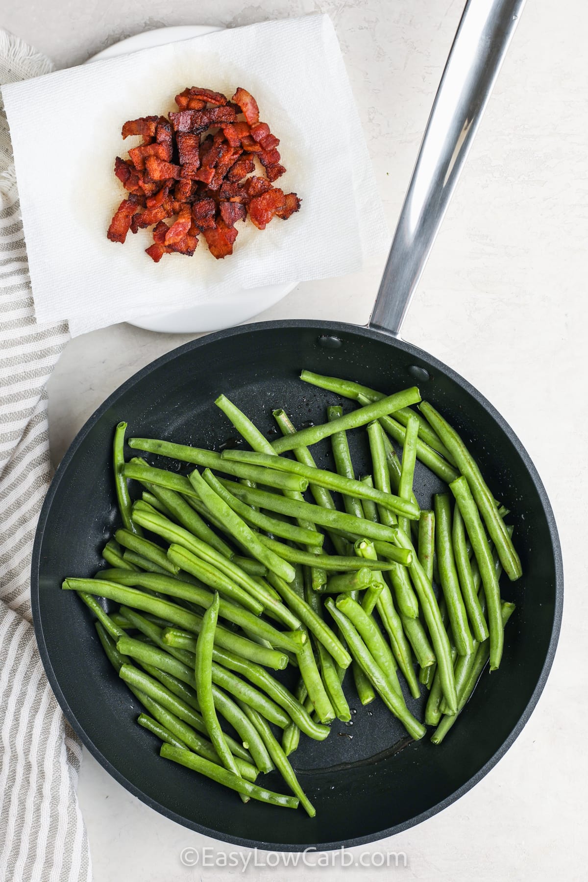 Bacon green beans combine crisp-tender vegetables with savory bacon for a side dish that shines. Cooking the beans in a bit of the leftover bacon drippings gives them a rich, smoky flavor without overwhelming their freshness. Finished with crumbled bacon and a pinch of salt and pepper, this dish is as easy as it is delicious. It’s low-carb, hearty, and totally crave-worthy. #easylowcarb frying green beans to make Bacon Green Beans