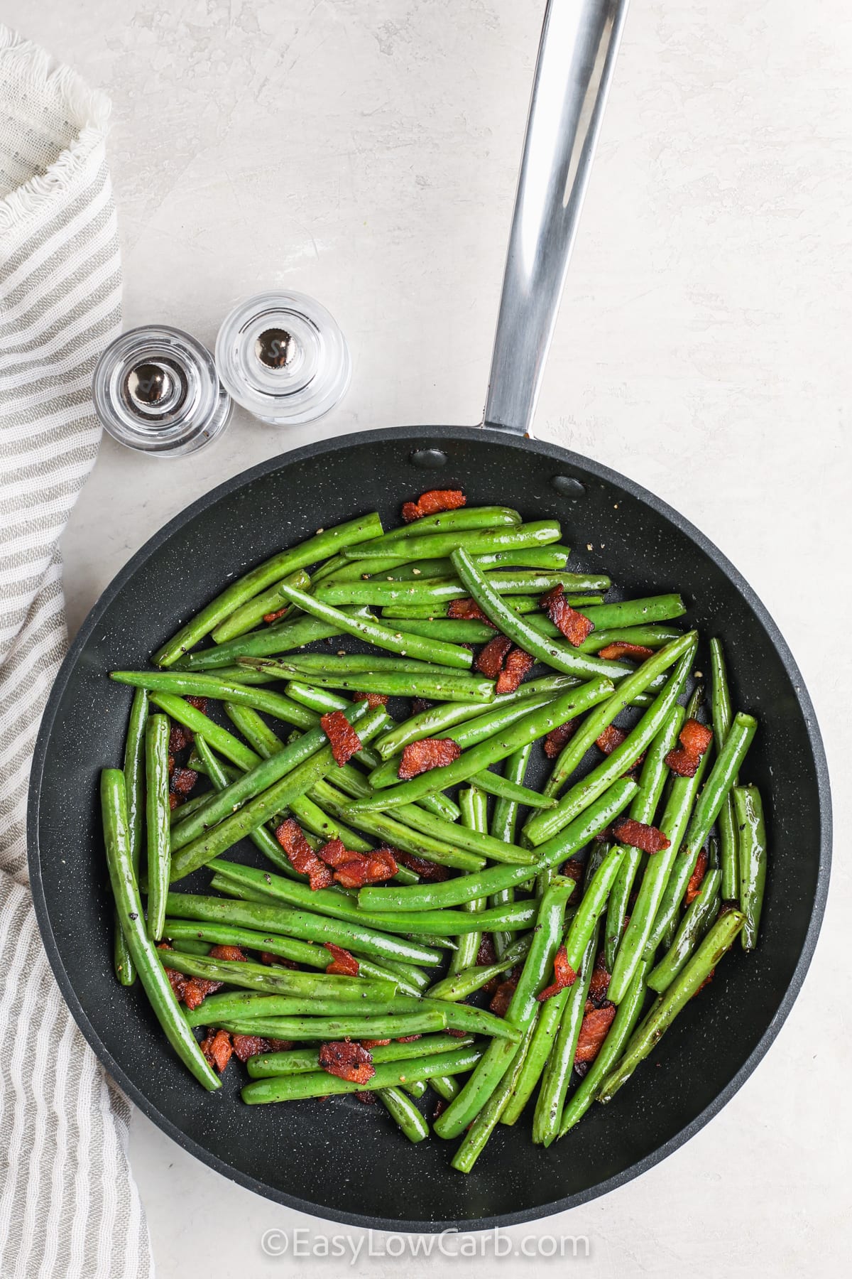 Bacon green beans are a simple, satisfying side dish that pairs perfectly with chicken, pork, or steak. Fresh green beans are sautéed in a touch of bacon drippings, then tossed with crispy bacon pieces for a delicious low-carb option that’s full of flavor. Ready in minutes and made in one pan, this easy recipe is perfect for busy nights or weekend meals. #easylowcarb Bacon Green Beans cooked in the pan