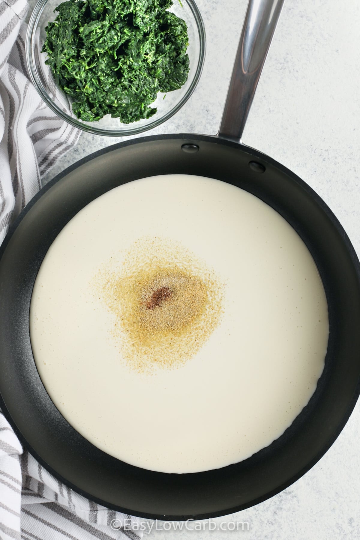 Enjoy this recipe for Creamed Spinach when you want a quick low carb side that is creamy and smooth. The spinach mixes with a seasoned cream sauce made with heavy cream and pantry spices, giving it steady flavor in every bite. It warms up easily and goes well with roasted meats, grilled chicken, or seafood. This stovetop method keeps things simple and gives reliable results each time. #easylowcarb adding ingredients to pan to make Easy Creamed Spinach