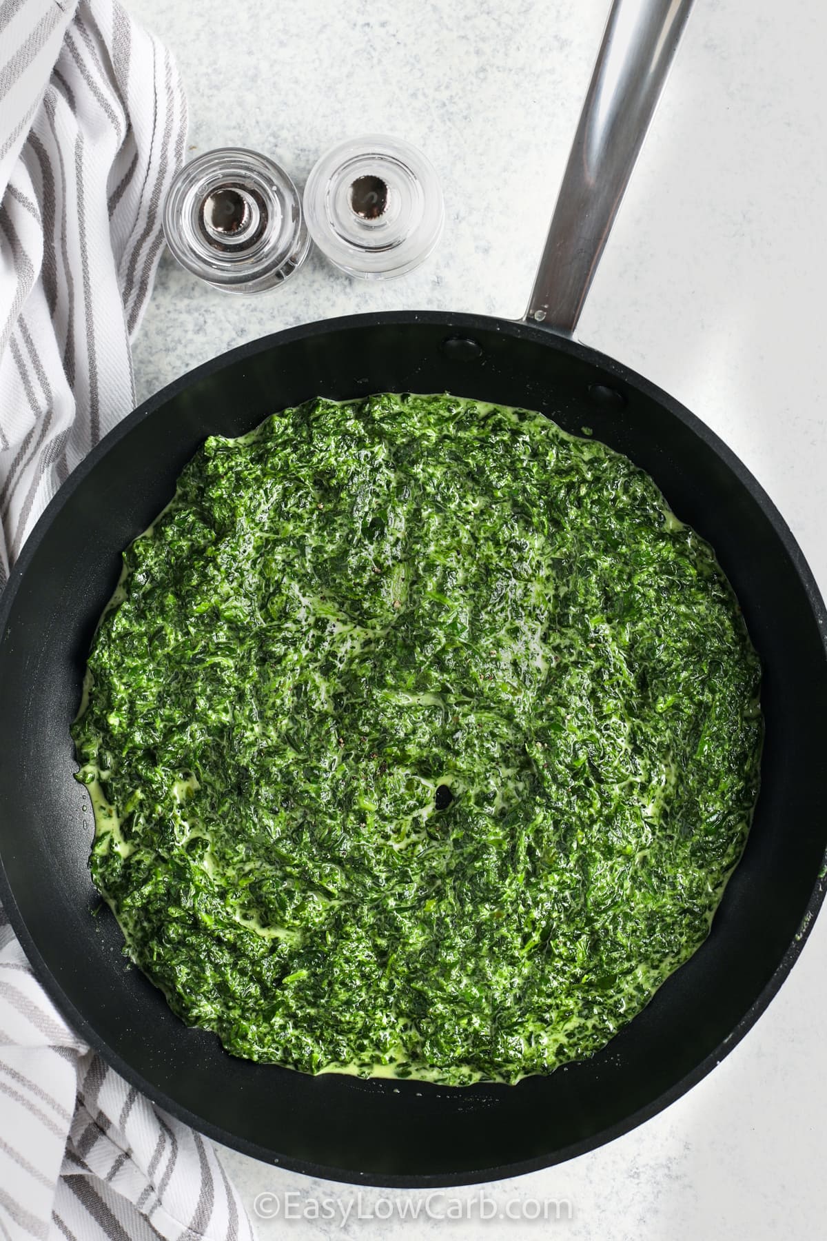 This recipe for Creamed Spinach creates a rich and velvety side dish made with tender spinach coated in a thick cream sauce. Heavy cream simmers with garlic powder, onion powder, and nutmeg to develop warm, savory flavor. The dish comes together quickly in one skillet and pairs perfectly with steak, chicken, or pork. It is a cozy, low carb favorite that works for both weeknight meals and special occasions. #easylowcarb Easy Creamed Spinach in the pan