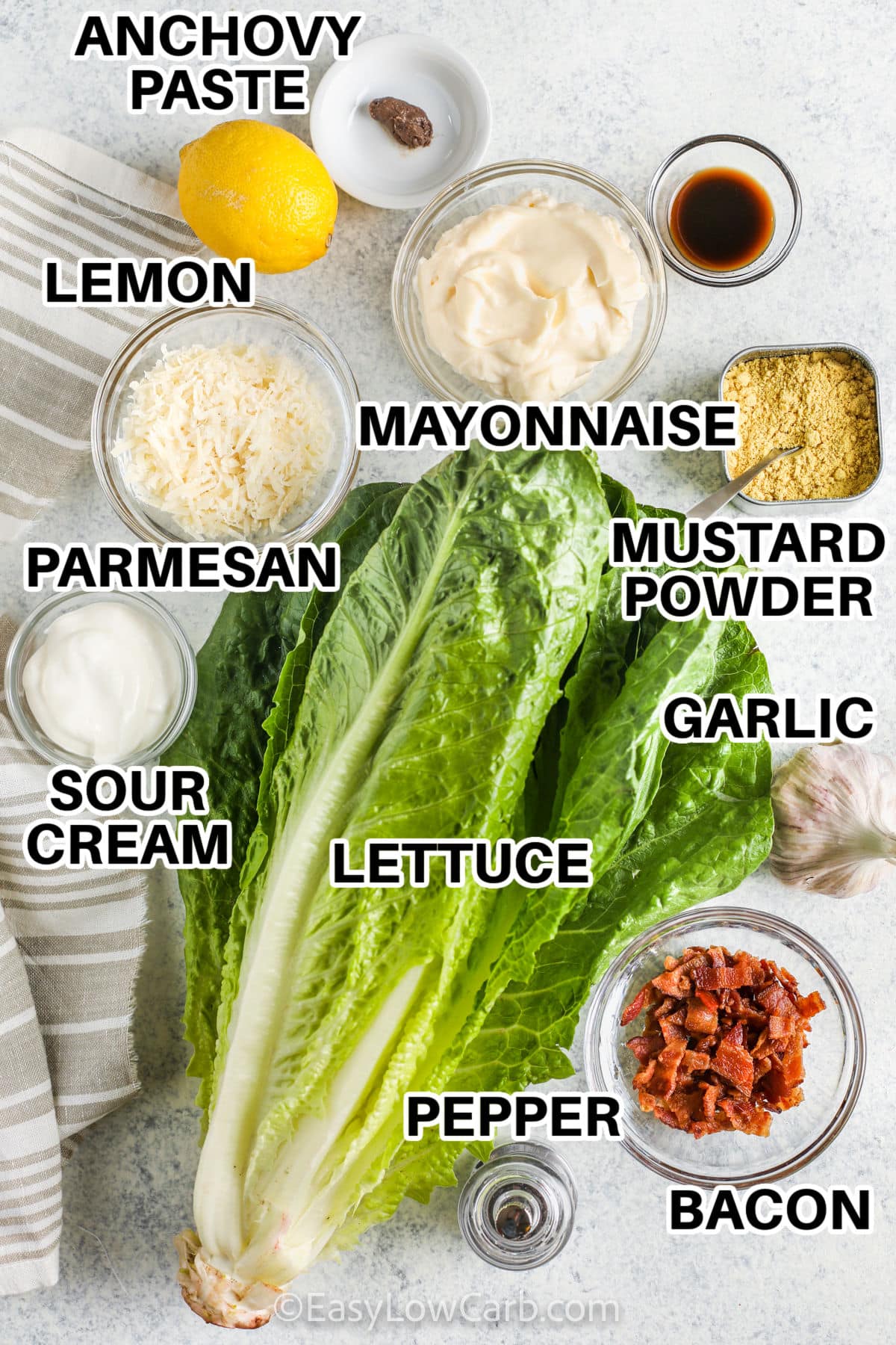 anchovy paste , lemon , mayonnaise , mustard powder , garlic , bacon , pepper , lettuce , sour cream and parmesan with labels to make Low Carb Caesar Salad Recipe