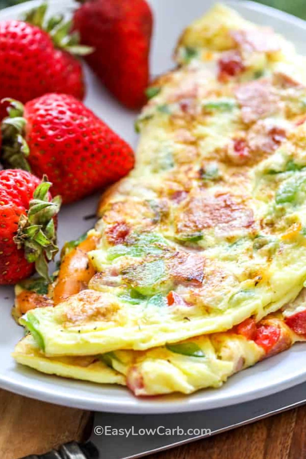 Denver omelet on a white plate with fresh strawberries on the side