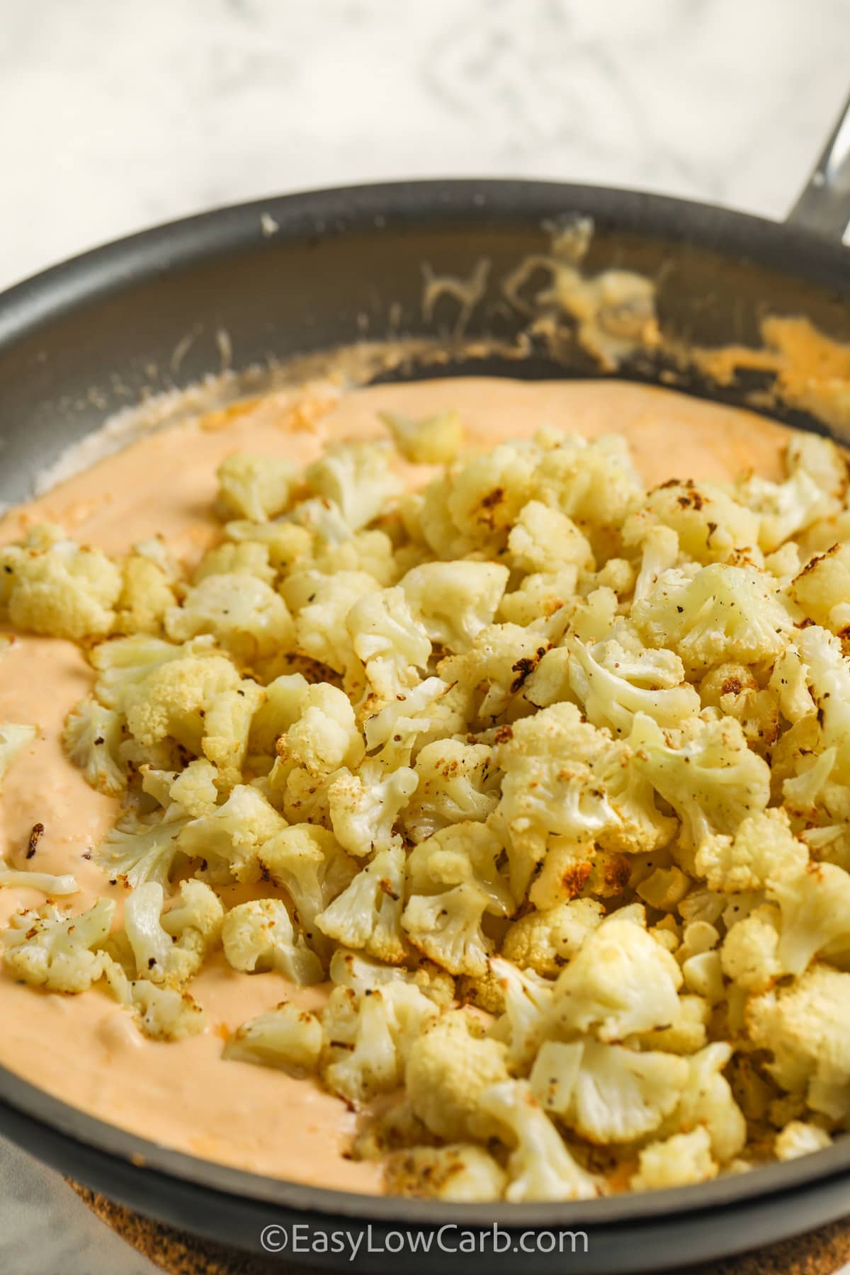 a sauce pan with cauliflower being added to a mac and cheese sauce